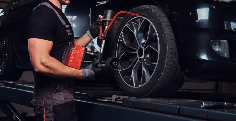 Muscular man is fixing car's wheel with special tool at auto service.